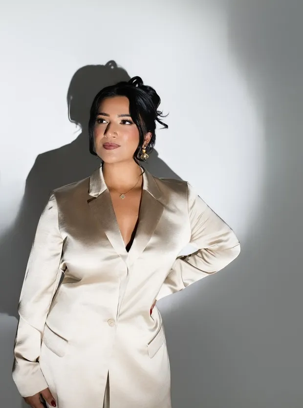 Saloni Singh, Esq., in a champagne suit under hard studio light, her shadow cast on the wall behind her
